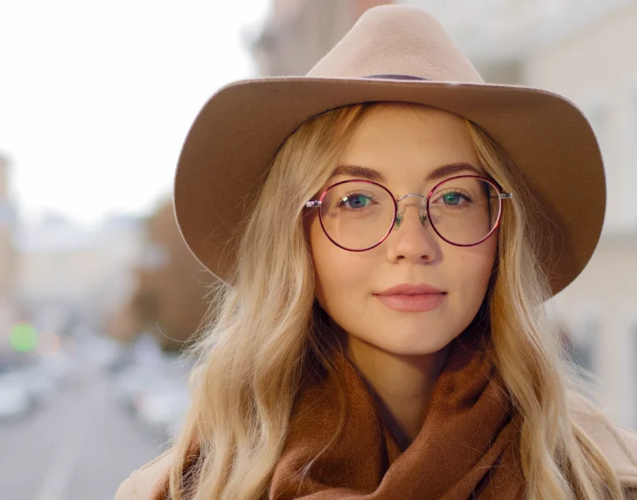 portrait-positive-young-woman-with-natural-makeup-attractive-caucasian-millennial-pretty-girl-looking-camera-closeup-female-with-long-blond-hair-smile-street-lady-with-glasses-hat-outdoors-min